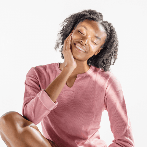 woman in pink shirt with beautiful, glowing skin smiling with eyes closed