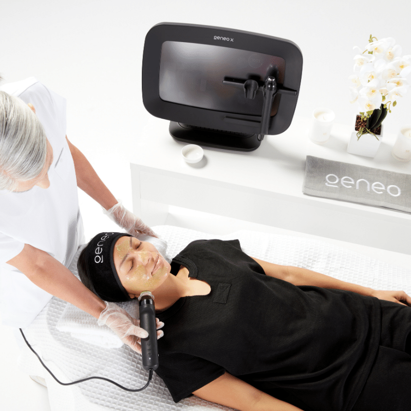 Woman in black receiving facial treatment from woman in white, using a Geneo X facial machine
